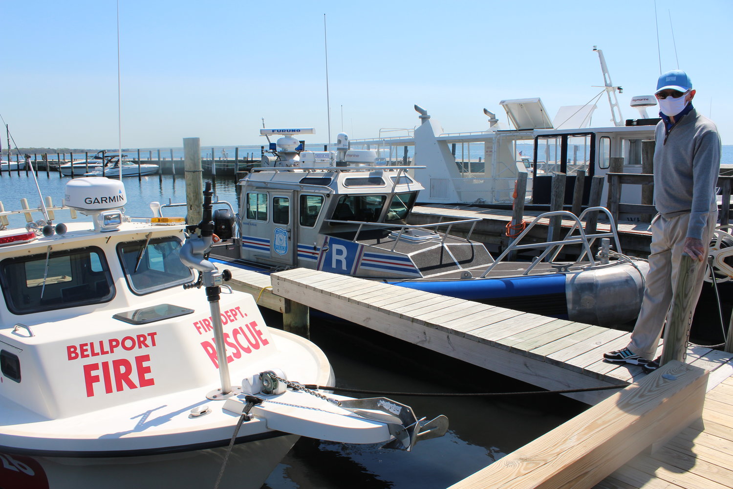 Bellport mayor Ray Fell stands by the Bellport Fire Department and Suffolk County Police Marine Unit boats. Federal funds requested would strengthen the dock’s points of departure for both agencies as well as South Country Ambulance in emergencies.